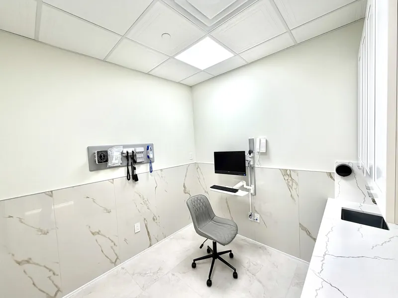 Examination room with marble-look porcelain wainscot, a quartz counter with sink and wall-mounted equipment