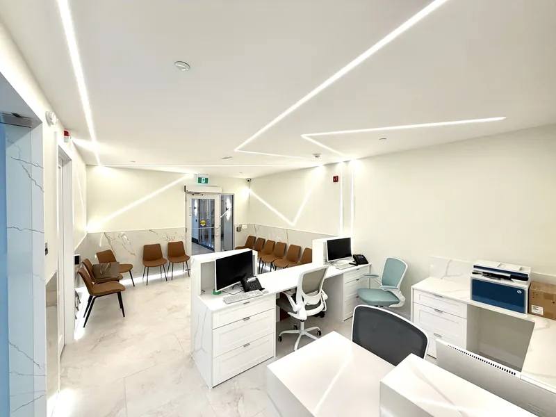 Front office with custom white millwork workstations and quartz counters, looking toward a waiting area lit by linear LED fixtures
